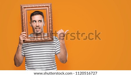 Handsome young man looking through vintage art frame pointing with hand and finger up with happy face smiling