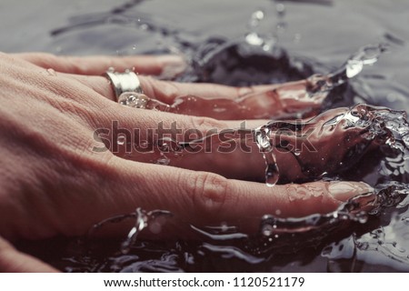 Young woman hand splashing in clean water, extreme close-up detail. Splash high-speed photography macro concept background. Female hand with wedding ring splashing water.  Royalty-Free Stock Photo #1120521179
