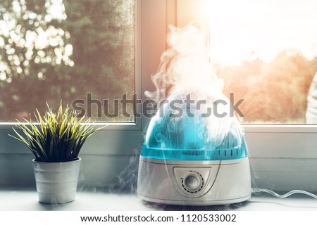 Air humidifier during work. The white humidifier moistens dry air. Improving the comfort of living in the home, apartment. Improving the well-being of people. Royalty-Free Stock Photo #1120533002