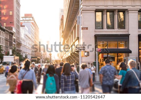 Diverse group of anonymous people walking down busy urban street with bright sunlight shining in the background in New York City