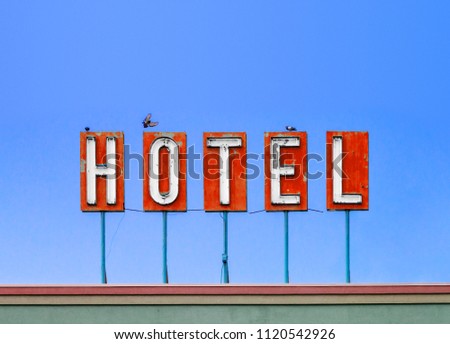 Red hotel sign on top of a dirty old motel isolated on blue sky background with birds