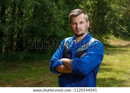 A man builder in a robe, overalls against the background of a green forest. copy space.