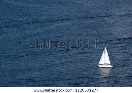 Nautical background of a white sailboat in bright sunlight, on dark blue ocean water, with space for text on left