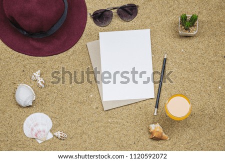 Flat lay, top view summer accessories Orange juice with note paper, hat, cactus and seashell on the beach