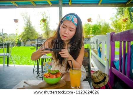 young happy and pretty digital nomad Asian Chinese woman taking picture of fruit salad with mobile phone networking on internet social media in healthy nutrition and travel blogger food review