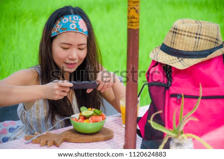 young happy and pretty digital nomad Asian Chinese woman taking picture of fruit salad with mobile phone for sharing on internet social media in healthy nutrition and travel blogger food review