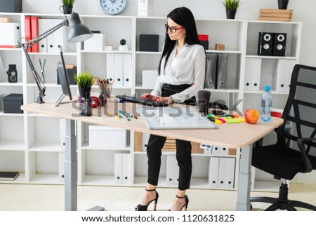 A young girl stands near a table and prints on the keyboard. Before the girl is a magnetic board and markers.