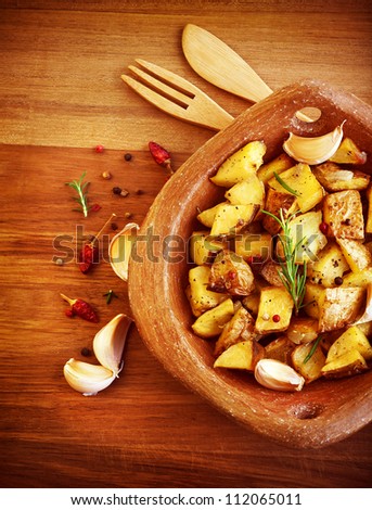 Picture of fried potato with garlic and spices on wooden table, baked quartered potato with vegetables serve in wooden plate with knife and fork, homemade french fries, restaurant dish