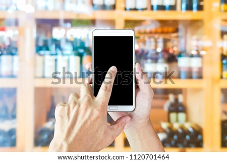 Man use mobile phone, blur image of wine shop as background.
