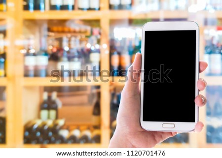 Man use mobile phone, blur image of wine shop as background.