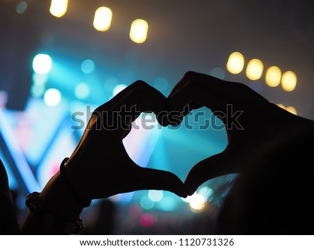 K-Pop music theme or Live concert background with silhouette hands of audience making heart shaped hand gesture for artist supporting on blurred background of a large stage with bokeh defocused lights
