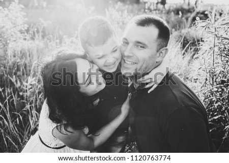 Happy young family spending time together outside in nature on vacation outdoors. Mom, dad and son sit in the grass. The concept of family holiday. Black and white photo.