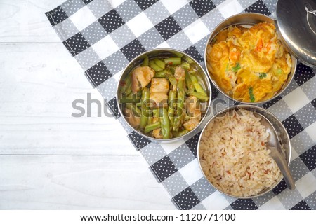 Antique stainless steel food carrier (Tiffin food container) and spoon on wood background. Set of food. Brown rice, Stir fried string bean and pork, Omelette with shrimp (Omelet). Copy space. Simple. Royalty-Free Stock Photo #1120771400