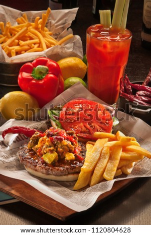 Mexican breakfast on the newspaper: steak, French fries, hot chili, paprika, lemon, lime, tomato drink in a glass with ice
