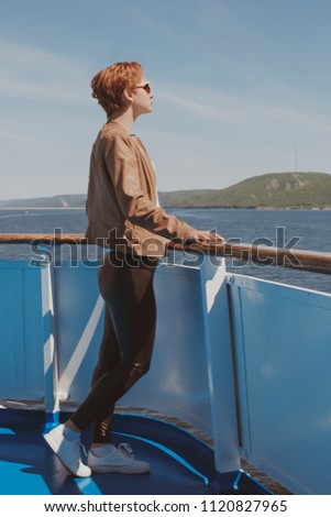 Young beautiful woman in sunglasses and orange hair, against the background of a river. Landscape. Cruise on the river, sea, travel. Positions for a snapshot. Observation deck.