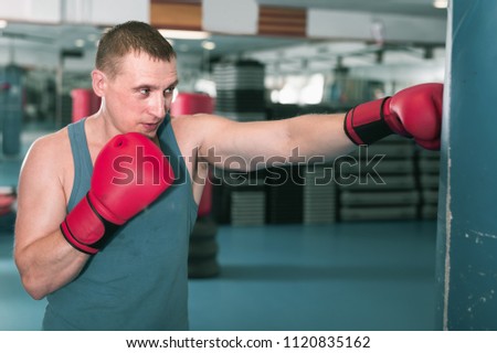 Adult man is training with punching bag in box gym