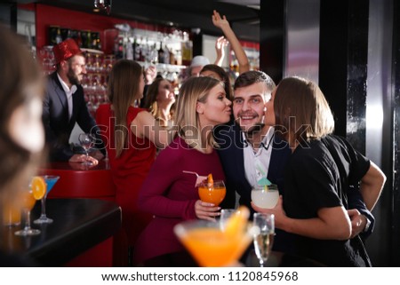 Guy getting friendly kiss on cheeks by attractive girls on cocktail party in bar