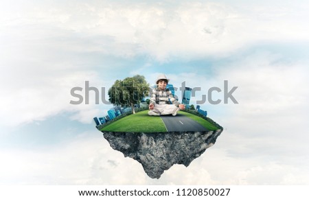 Young little boy keeping eyes closed and looking concentrated while meditating on flying island in the air with cloudy skyscape on background. 3D rendering.