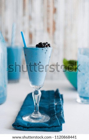 Blue Majik smooothie on tall glass with colored straw, over a blue colored wooden board against a clear background