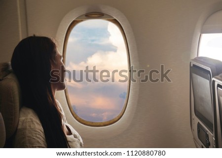 A woman relaxes on the plane while flying, to go on vacation, on her comfortable seat and from the window you can see the clouds of the sky. Concept of: travel, vacation and transport. Royalty-Free Stock Photo #1120880780