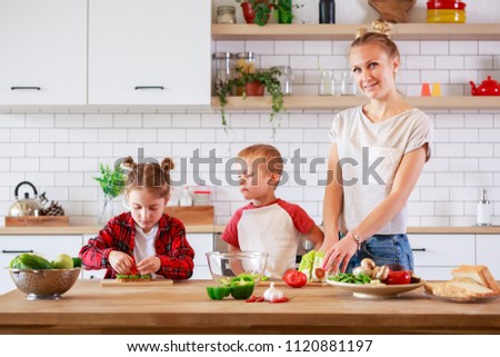 Picture of young mother with daughter and son cutting vegetables at table