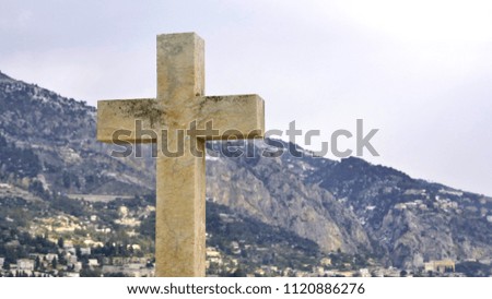A stone cross at the background of a small city and mountains.