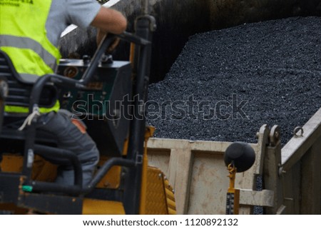 Industrial pavement machine laying fresh asphalt on road construction.