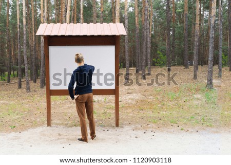 A young guy looks at the information stand in a pine forest in the city Park. Mock-up stand