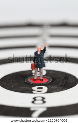 Miniature people: businessman standing on dartboard target center idea of financial and business goal