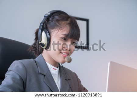 Asian Young woman friendly operator or call center agent with headsets working in call centre. Smiling to customer support operator at her computer at work office. Royalty-Free Stock Photo #1120913891