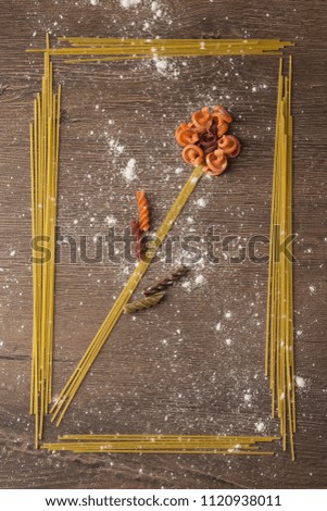 Conceptual picture with pasta in the kitchen. A flower is laid out of the food in a frame and sprinkled with flour