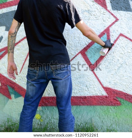 A young hooligan paints graffiti on a concrete wall. Illegal vandalism concept. Street art