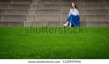 Beautiful woman sitting on stone steps in front of the bright green grass. Fashionable photo.