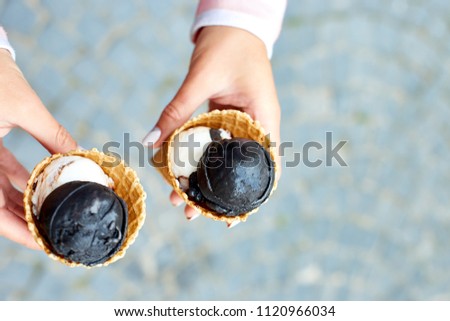 Female hand holding two charcoal and vanila ice cream in waffle cone on city background. Italian traditional ice cream gelato. Copy space. Top view.