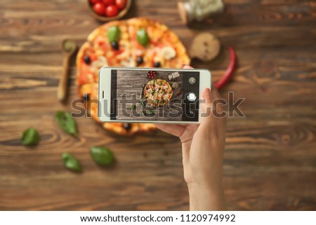 Woman taking photo of delicious Italian pizza with mobile phone