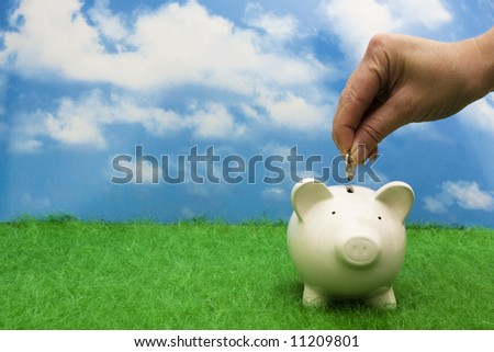 Coin bank sitting on grass with hand putting in a coin Royalty-Free Stock Photo #11209801