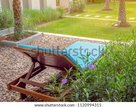Wooden Relaxing Sunbed on Gravel and Green Grass Floor with Coconut Palm Tree in The Garden