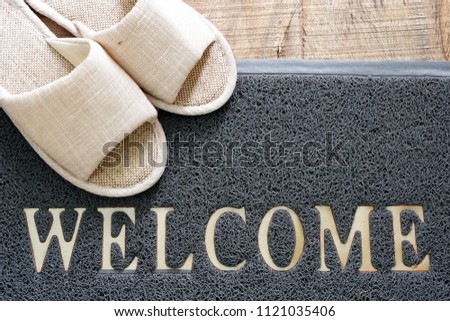  Cream color soft slipper and gray welcome mat on natural wooden floor,top view for copy space