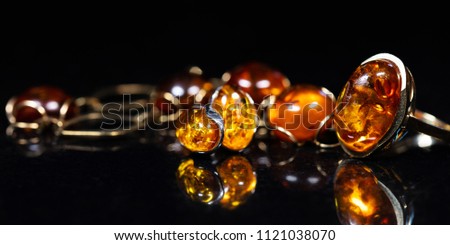 panorama of jewelry with amber stones, amber necklace ring and earring and pendant with noble metal like gold, in front of a black background on a black stone with reflection Royalty-Free Stock Photo #1121038070