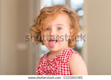 Beautiful blonde child with blue eyes smiling with tongue out at home.
