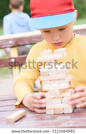 Caucasian kid is playing wood blocks tower game for practicing physical and mental skill. Emotional photos.