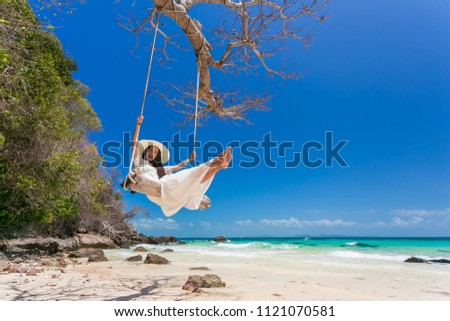 A beautiful woman wearing a hat and white dress is enjoying the sea swing at Mai Ton Island, Phuket, Thailand.