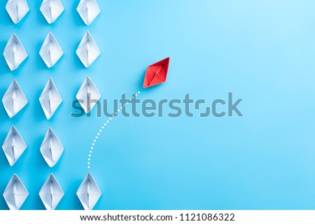 Group of white paper ship in one direction and one red paper ship pointing in different way on blue background. Business for innovative solution concept. Royalty-Free Stock Photo #1121086322