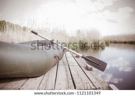 An old pier, a calm pond, a lake, a river. A rubber boat with an oar. Summer holidays in the countryside, outside the city. Retro style, muted tone, vignetting.