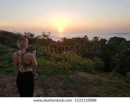 photographer taking picture of sunrise at ocean shore using professional camara and tripod