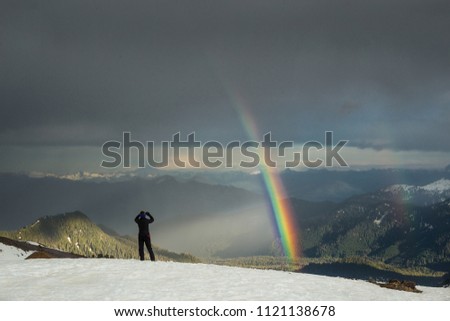 Double rainbow over the sky in the mountains and a girl taking a picture of it. Mt. Baker recreation area, Washington, USA.