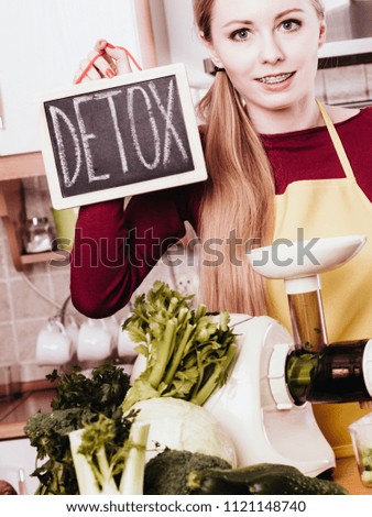 Drinks good for health, diet breakfast concept. Young woman in kitchen making green healthy vegetable smoothie juice holding detoxsign