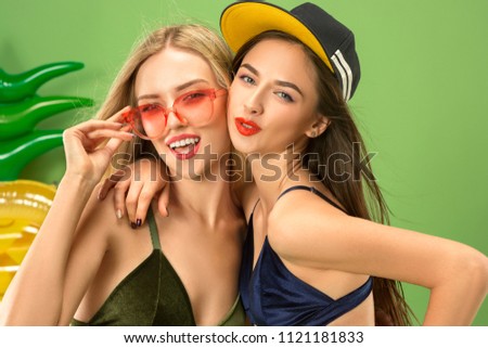 Cute girls in swimsuit posing at studio. Summer portrait caucasian teenagers on a green background. Concept of summer, summertime, recreation, break, vacation, travel.