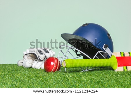 Cricket equipment with bat, ball, helmet and gloves on grass with green background.