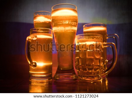 Creative concept. Beer glasses on table at dark toned foggy background with blurred view of flag of Russia. Support your country with beer concept. Selective focus